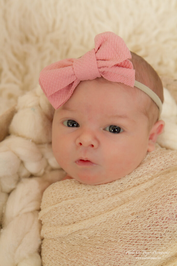 Newborn Lucy Roberts wrapped in a blush pink swaddle, lying peacefully on a soft cream blanket.
