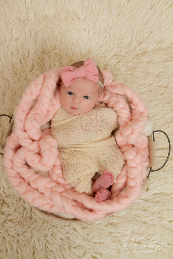 Newborn Lucy Roberts wrapped in a blush pink swaddle, lying peacefully on a soft cream blanket.
