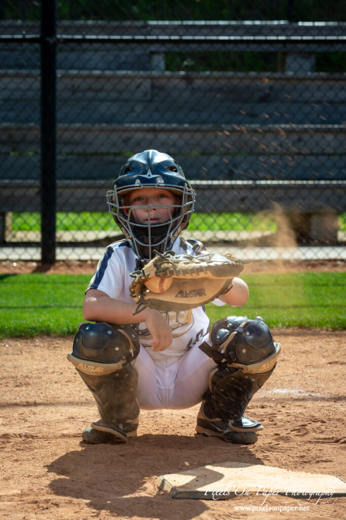 Young baseball catcher from NWNC Elite 8U posing with cap and glove on the field